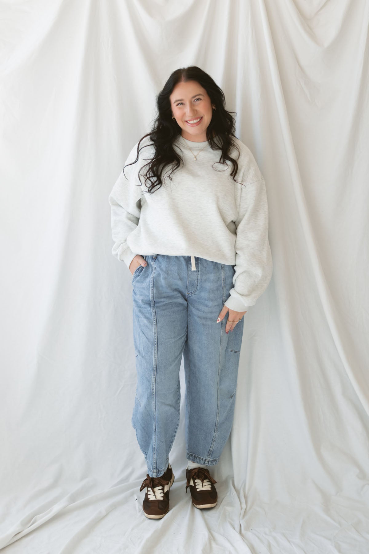 Model wearing the oversized grey crew neck sweatshirt. Model has it styled with a pair of barrel jeans and sneakers for a casual everyday look.