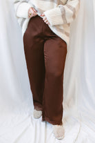 Brown satin wide-leg pants for women featuring delicate lace trim, a mid-waisted silhouette, and a smooth satin finish for elevated everyday styling.