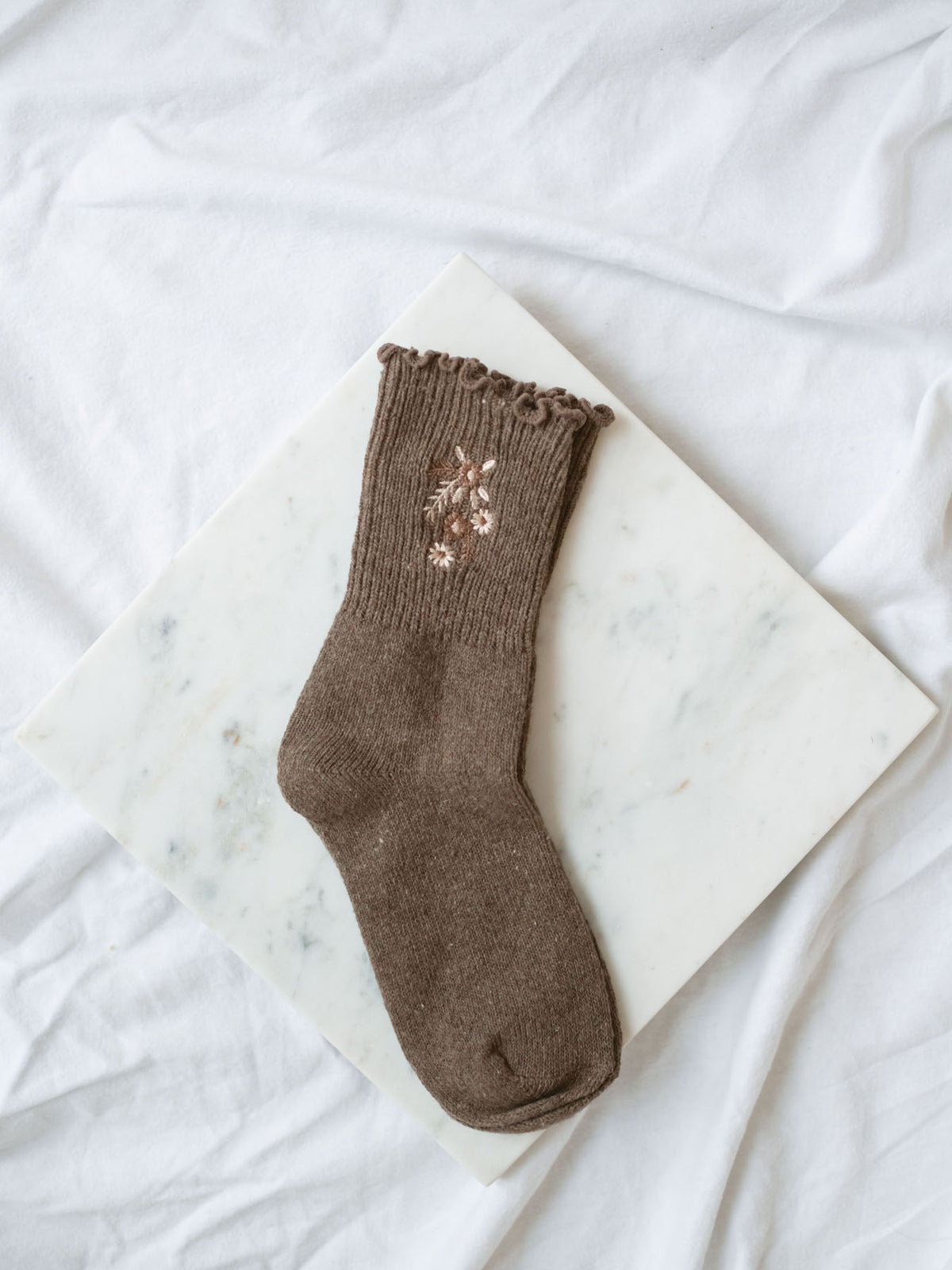 Dark coffee colored socks with floral embroidered detail sitting on marble board. 