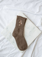 Dark coffee colored socks with floral embroidered detail sitting on marble board. 