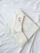 White floral embroidered detail socks laying on marble board. 