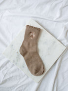 Light coffee socks with floral embroidery detail sitting on marble board. 