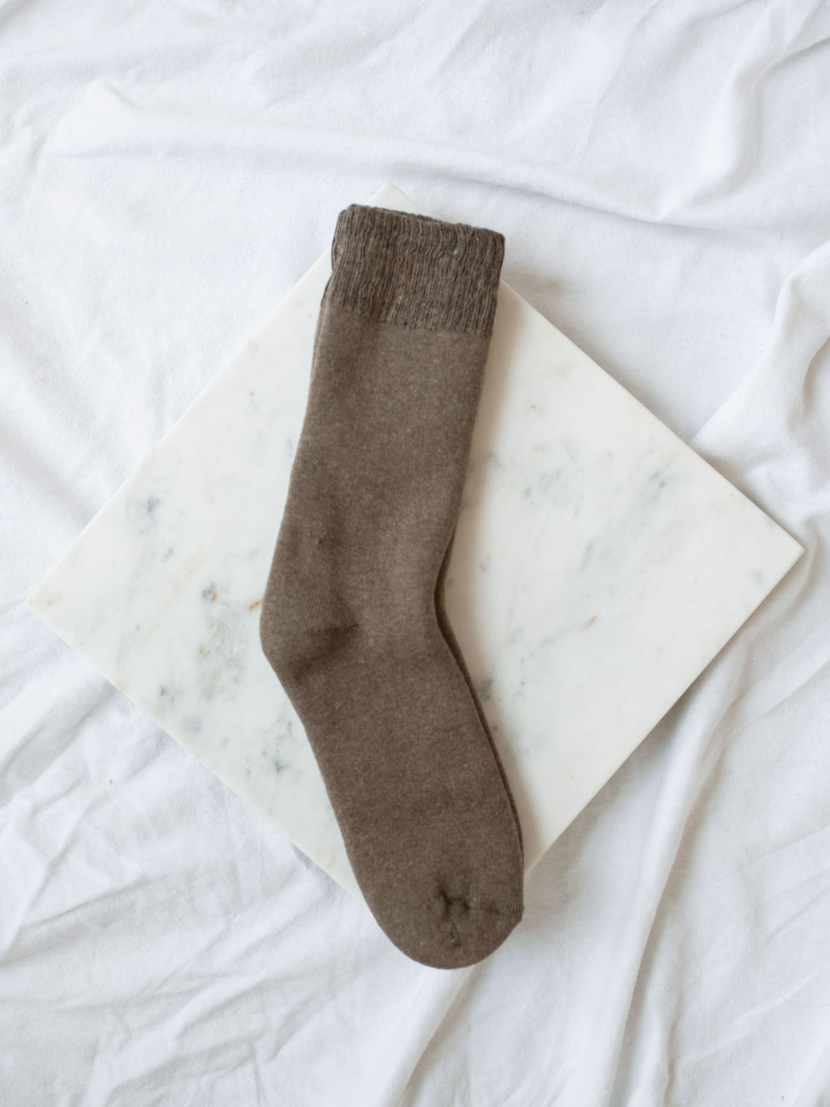 Coffee colored boot length sock laying on marble board.
