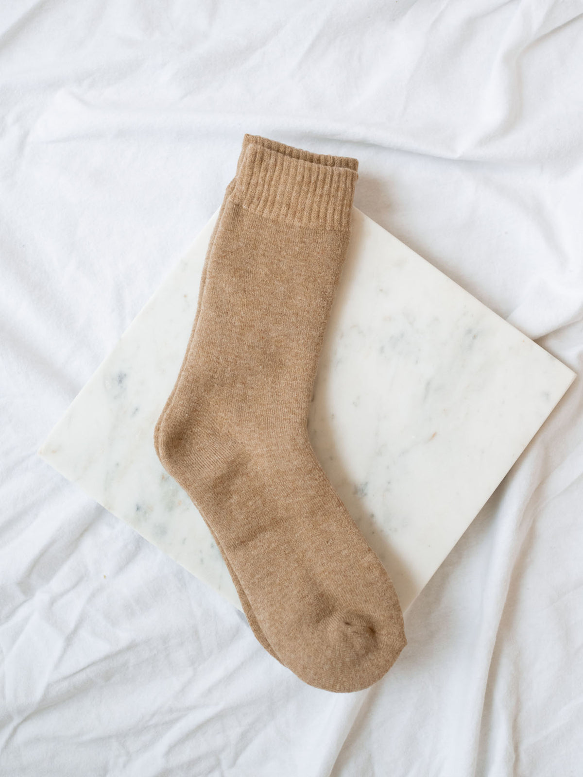 Light Coffee colored boot length sock laying on marble board.