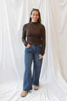 Chocolate brown long-sleeve knit turtleneck top for women featuring ruched waist detailing, a softly shaped silhouette, and an elevated everyday design.