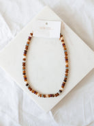 Mixed bead necklace in brown and tan laying on marble board. 