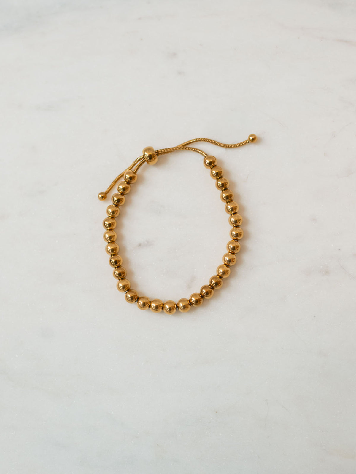 Gold beaded adjustable bracelet in medium size laying on marble board. 