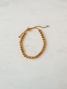 Gold beaded adjustable bracelet in medium size laying on marble board. 