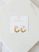 U-shaped gold hoops on white card laying on white marble board. 