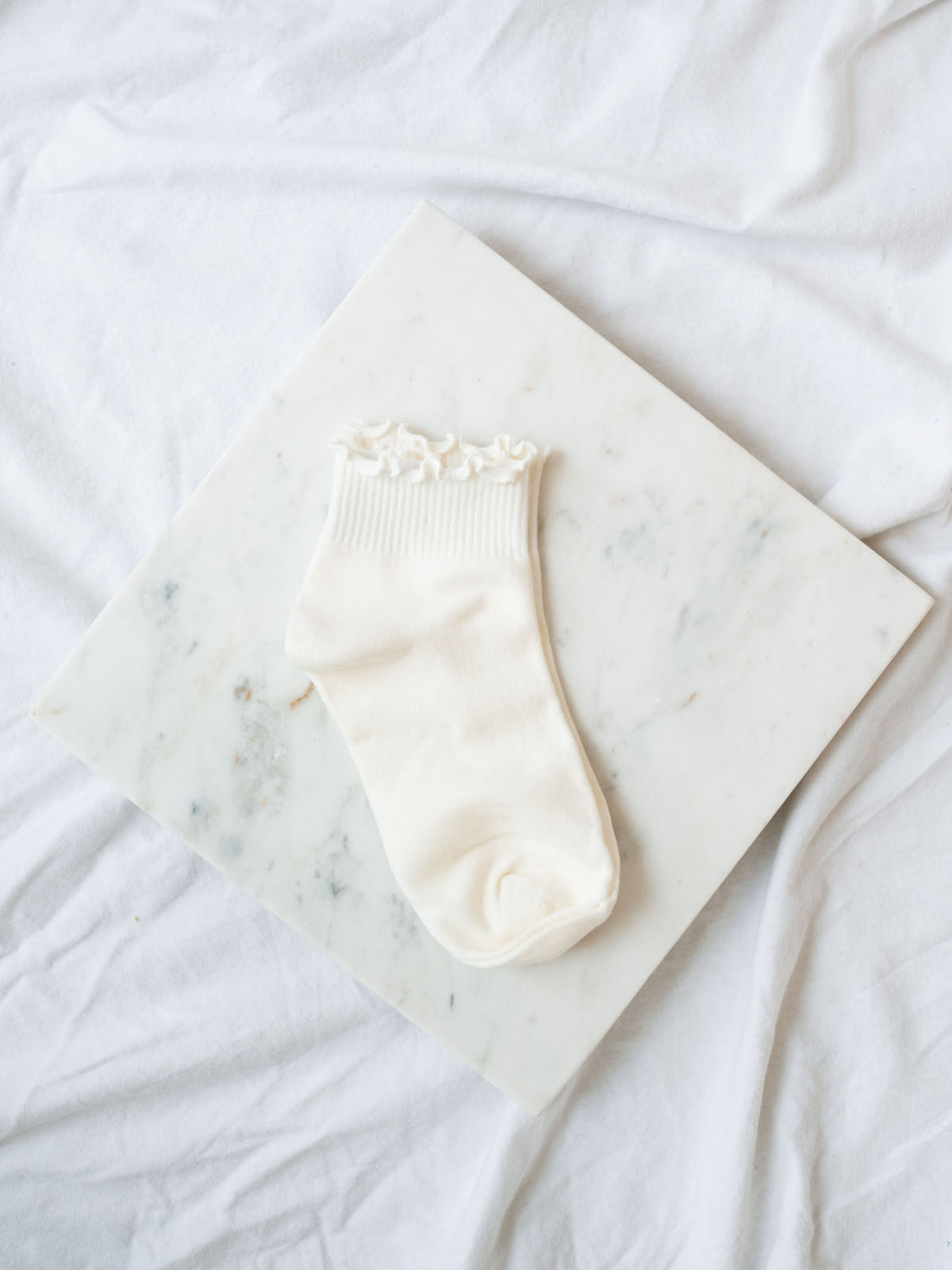 Cream ruffle ankle sock laying on marble board. 