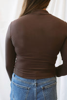 Chocolate brown long-sleeve knit turtleneck top for women featuring ruched waist detailing, a softly shaped silhouette, and an elevated everyday design.