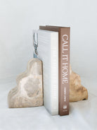 The set of beige marble scalloped edge bookends sitting with two books between them against a white linen backdrop. 