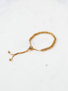 Gold beaded adjustable bracelet in medium size laying on marble board. 