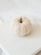 Cream knit filler pumpkin sitting on white marble board. 