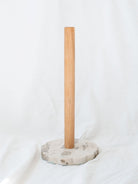 Wood and marble base paper towel holder sitting in front of a white linen backgrop. 