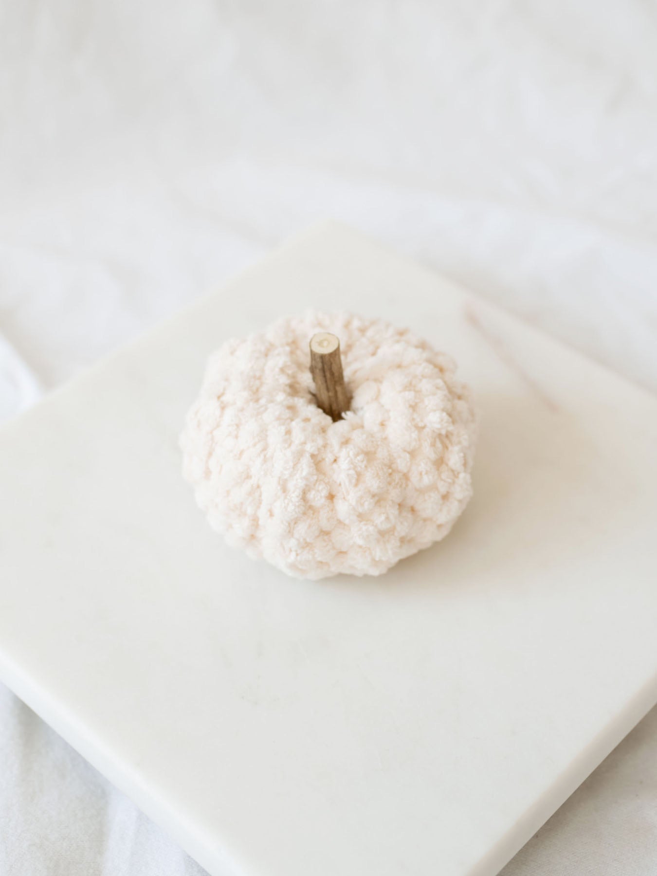 Cream velvet filler pumpkin sitting on white marble board. 