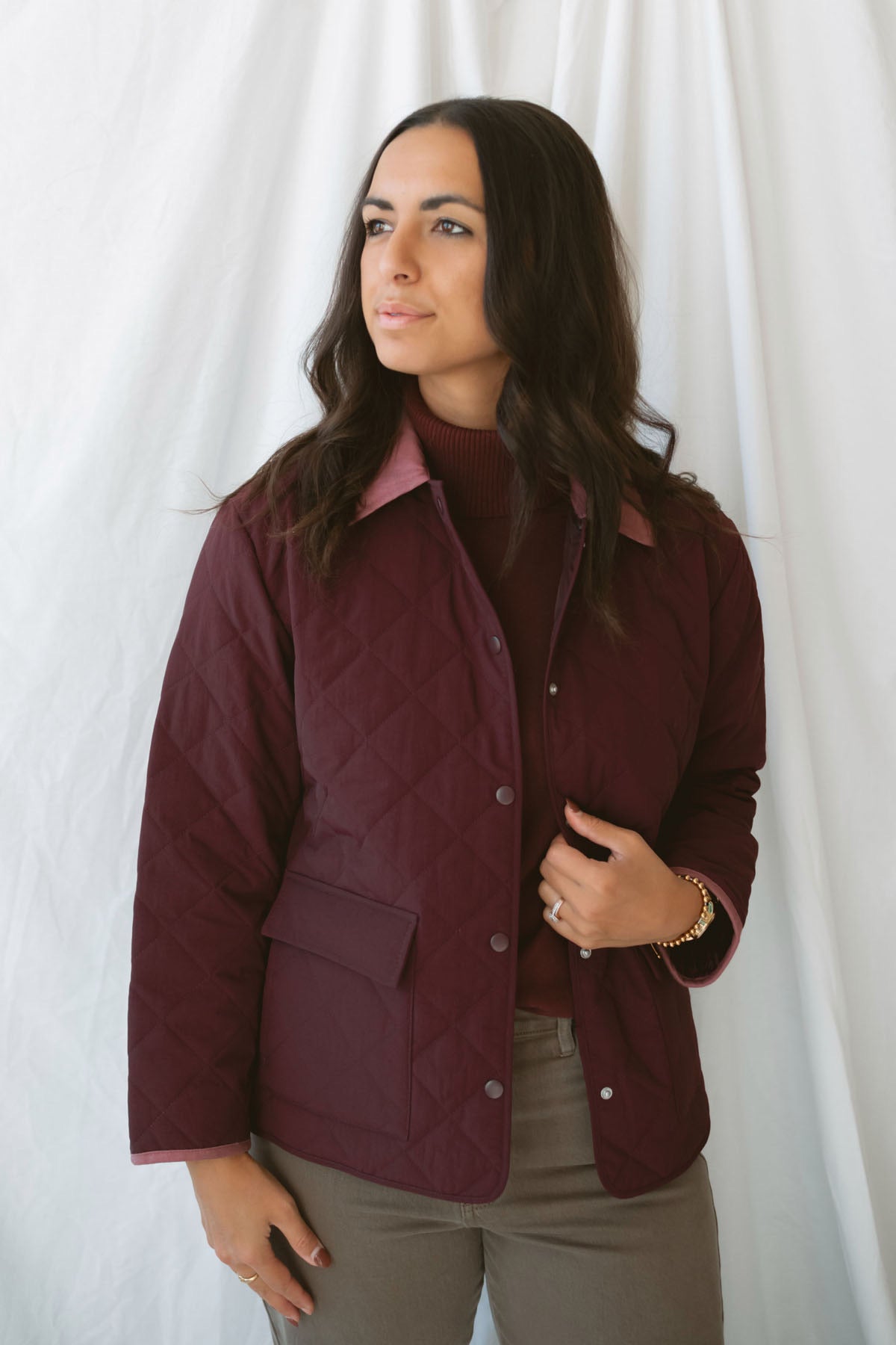 Model is wearing a quilted two tone jacket in burgundy. 