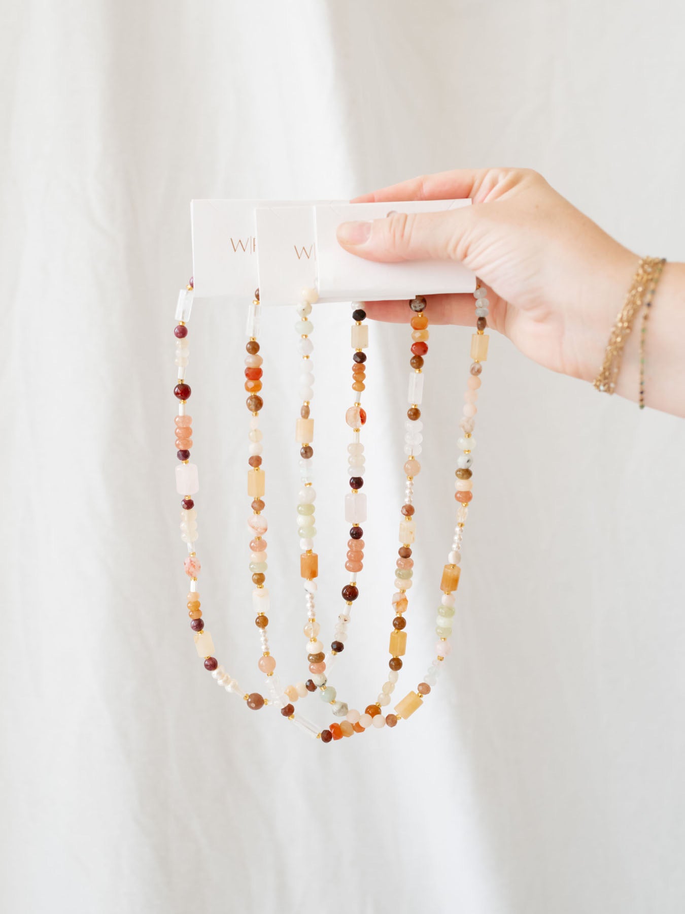 3 of the surprise beaded necklaces held up together in front of white linen backdrop