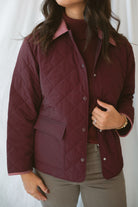 Model is wearing a quilted two tone jacket in burgundy. 