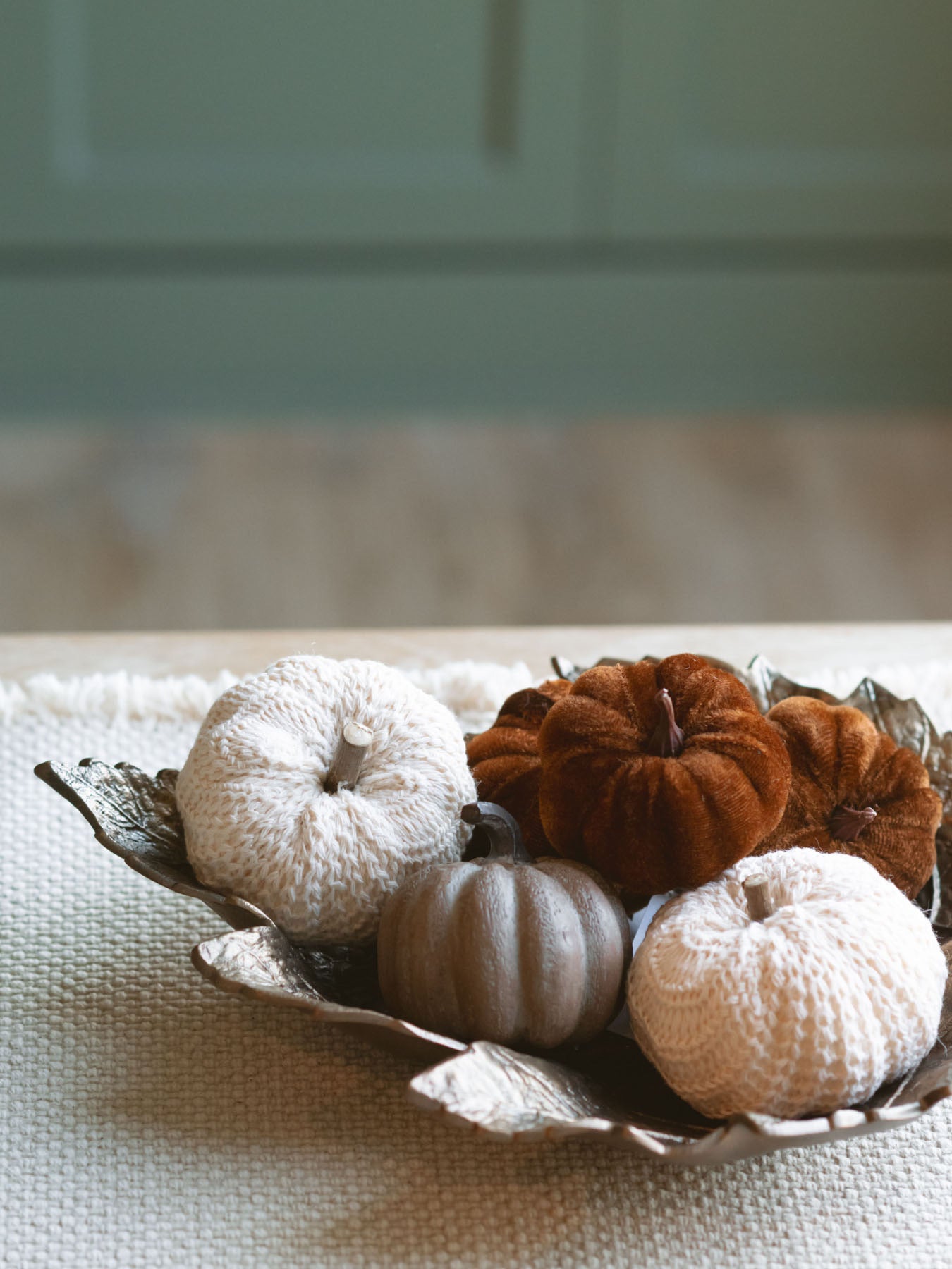 Antique gold leaf dish filled with small textured pumpkins sitting on a shelf. 