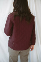 Model is wearing a quilted two tone jacket in burgundy. 