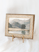 The gold straight back table top easel holding framed artwork. 