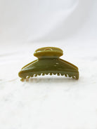 Green glossy fan shaped claw clip sitting on white marble board. 