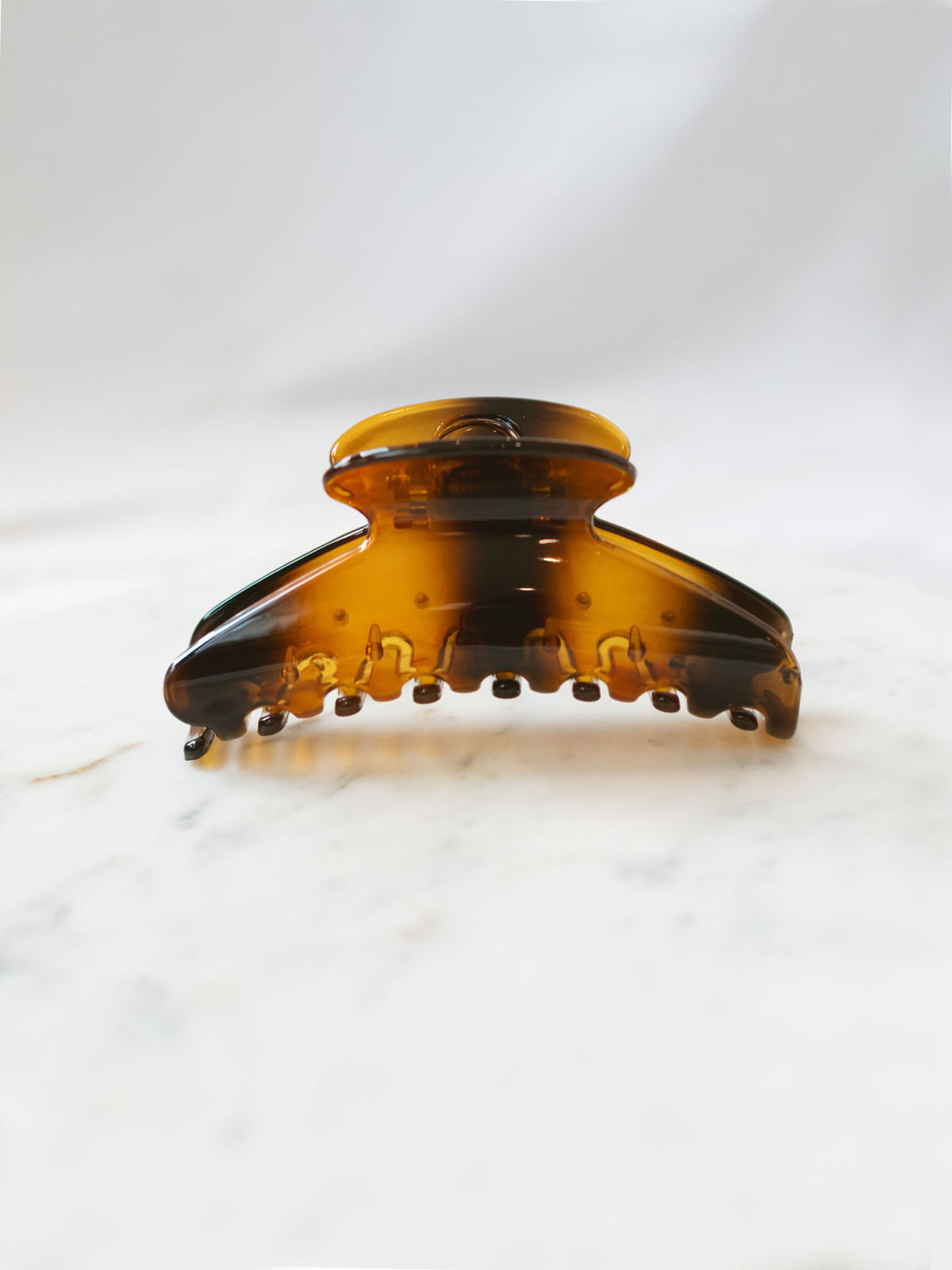 Brown glossy fan shaped claw clip sitting on white marble board. 