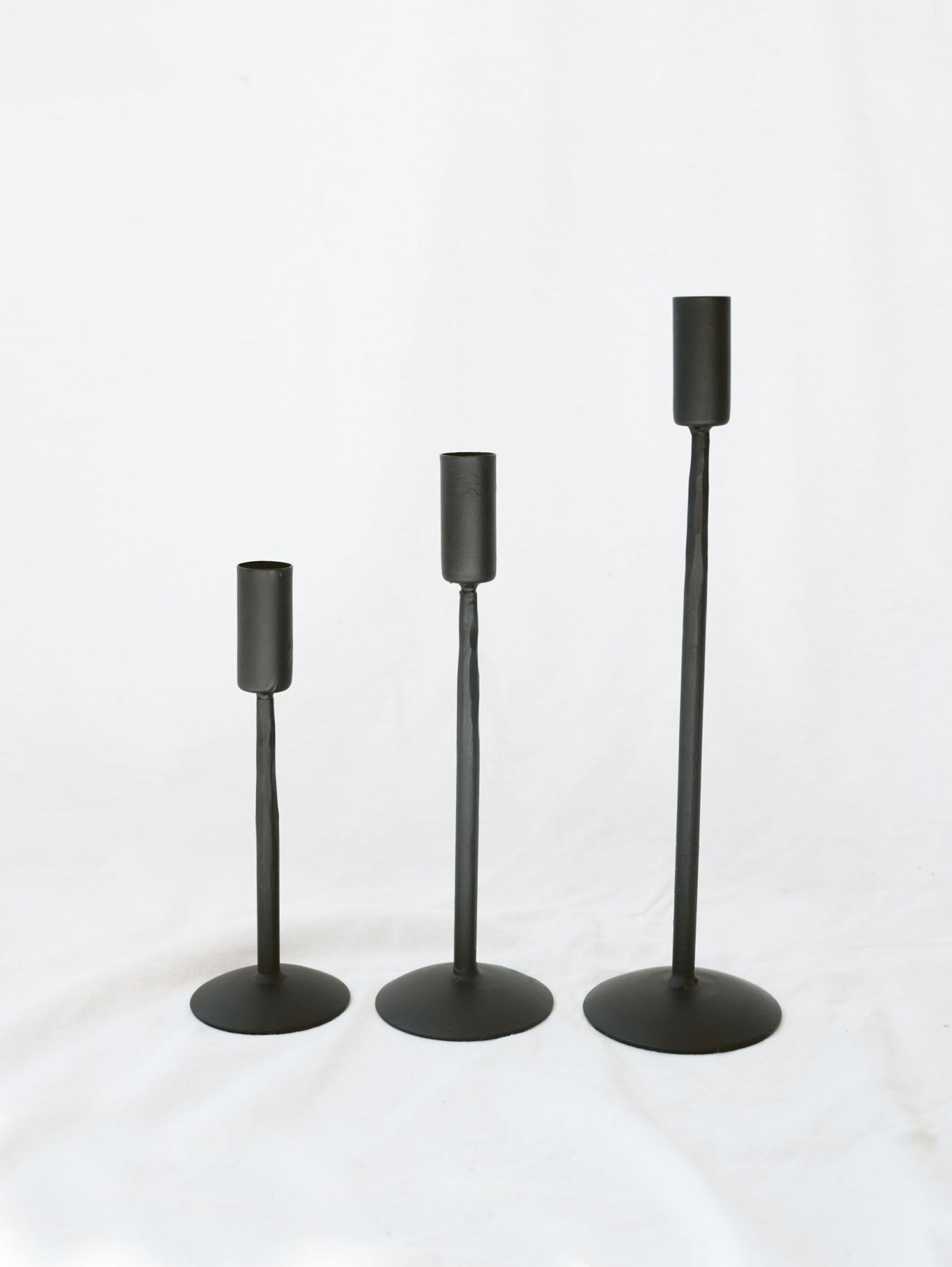 The three sizes of black candle stick holders sitting next to each other going from shortest to tallest. Simple, timeless, and chic home decor option. 