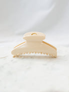 Cream/white glossy fan shaped claw clip sitting on white marble board. 