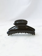 Black glossy fan shaped claw clip sitting on white marble board. 