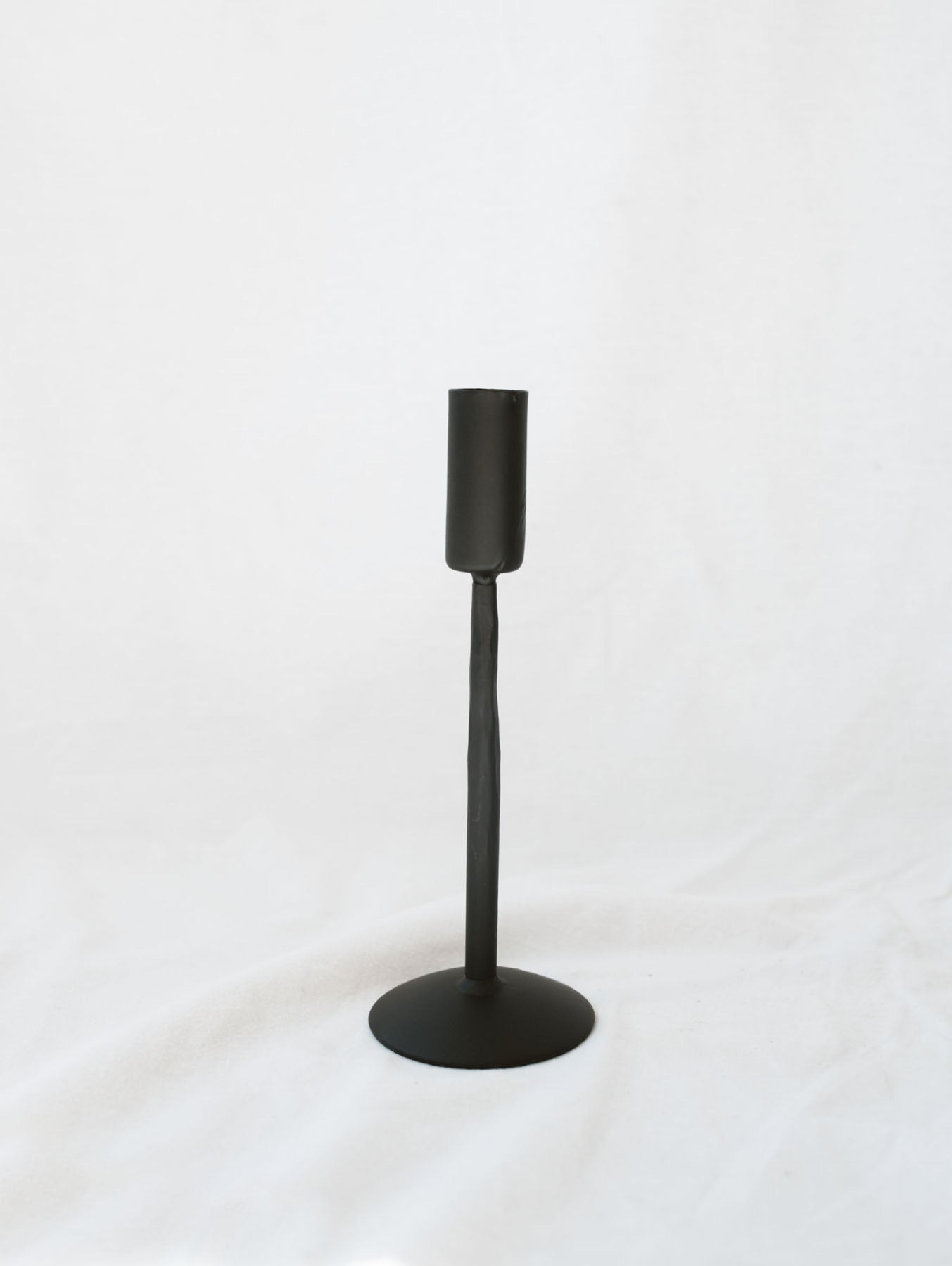 Smallest size black candle stick holder sitting on a white linen backdrop. Simple, timeless, and chic home decor option. 