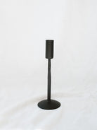 Smallest size black candle stick holder sitting on a white linen backdrop. Simple, timeless, and chic home decor option. 