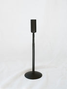 Middle size black candle stick holder sitting on a white linen backdrop. Simple, timeless, and chic home decor option. 
