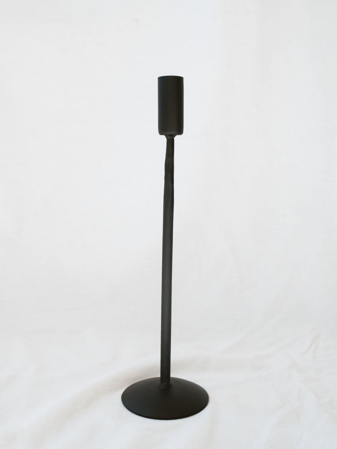 Tallest size black candle stick holder sitting on a white linen backdrop. Simple, timeless, and chic home decor option. 