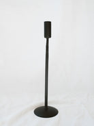 Tallest size black candle stick holder sitting on a white linen backdrop. Simple, timeless, and chic home decor option. 