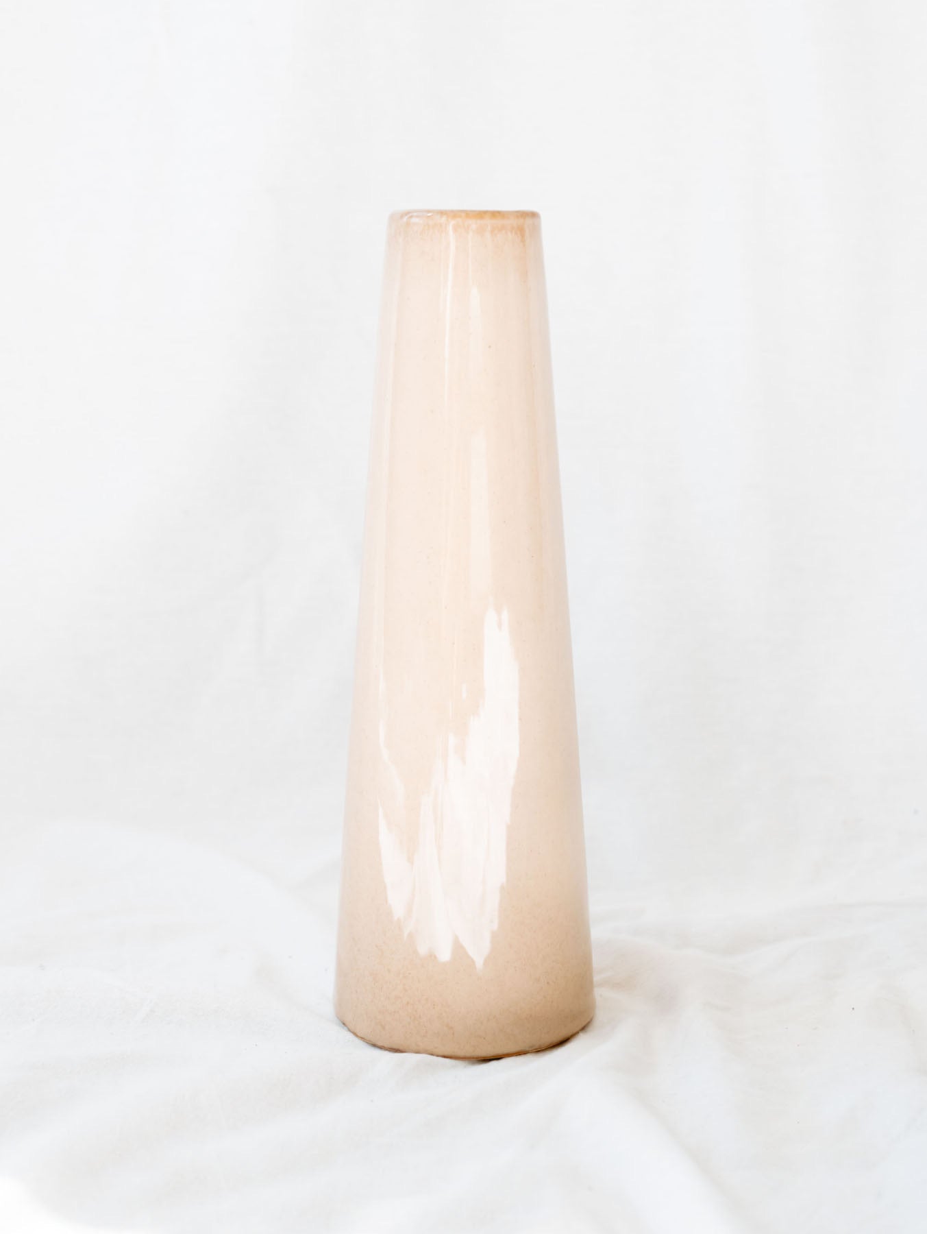 Narrow mouth tri color glazed artisan vase standing against a white linen backdrop. 