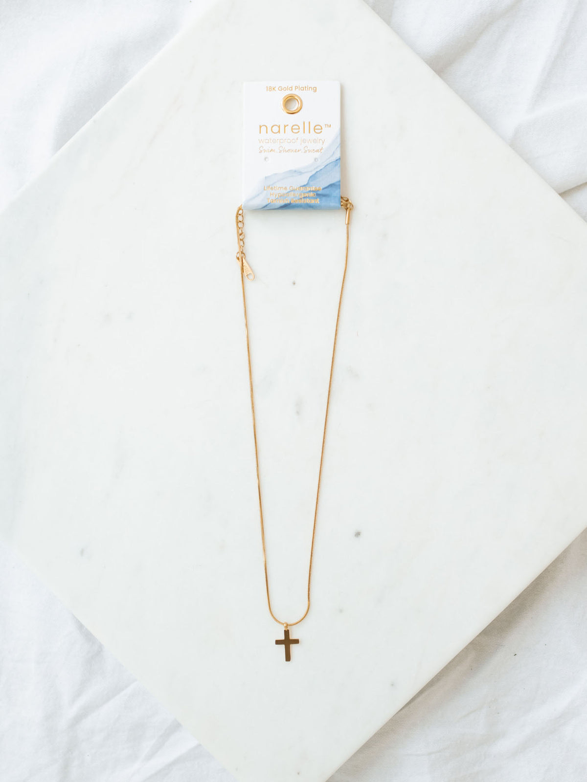 Cross necklace with snake chain in gold laying on white marble board.