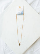 Cross necklace with snake chain in gold laying on white marble board.