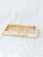 Side view of the beige marbled vanity tray laying on white linen backdrop. 