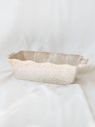 Side view of beige scallop edge baking dish on white linen backdrop.