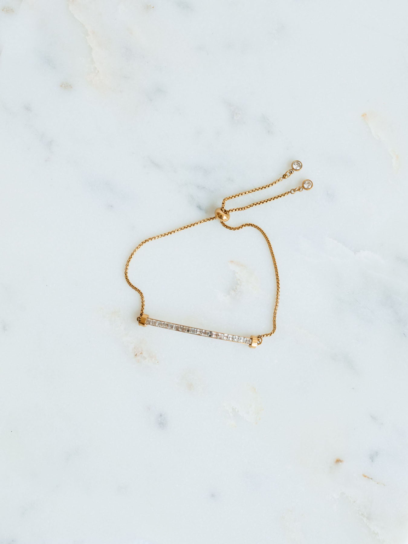 Montessa gold adjustable sparkle bar detail bracelet laying on marble board. 