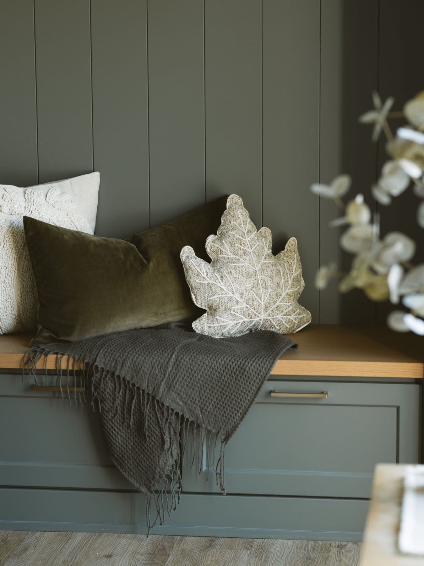 Olive green waffle knit throw blanket styled on a bench with other pillows for a cozy moment. 