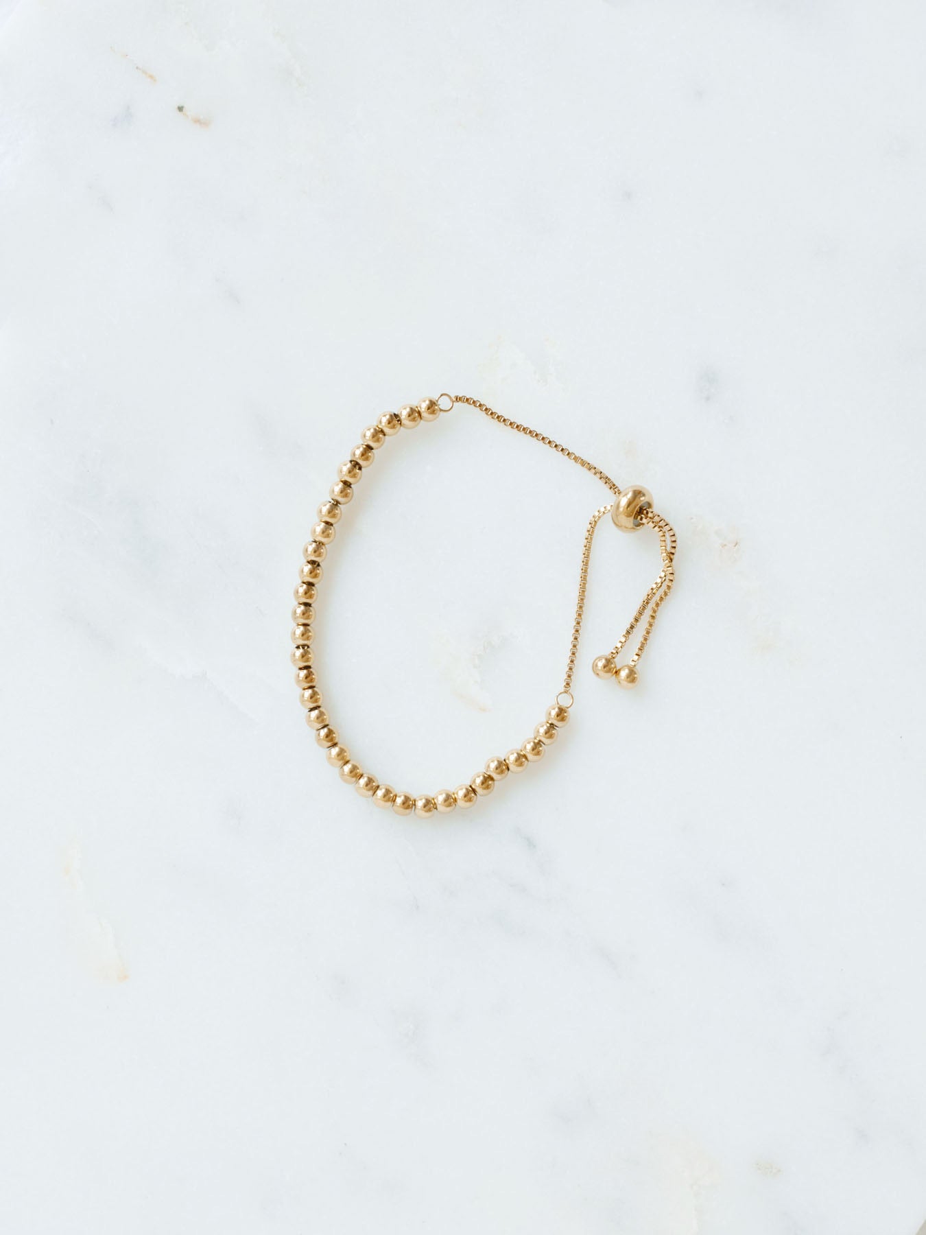 Gold beaded adjustable bracelet in medium size laying on marble board. 