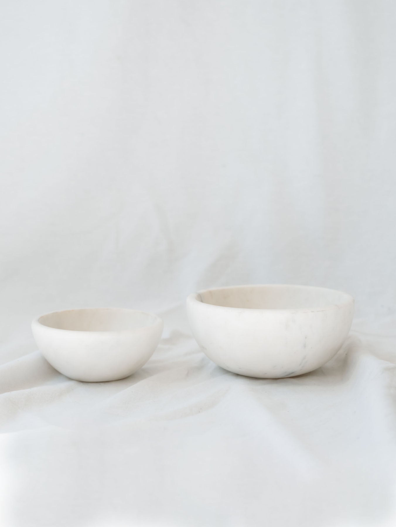 Two different sized marble bowls sitting next to each other in front of a white linen backdrop. 