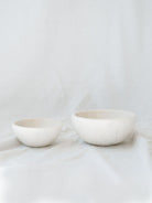 Two different sized marble bowls sitting next to each other in front of a white linen backdrop. 