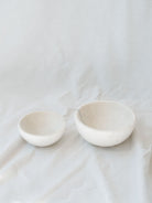 Two different sized marble bowls sitting next to each other in front of a white linen backdrop. 
