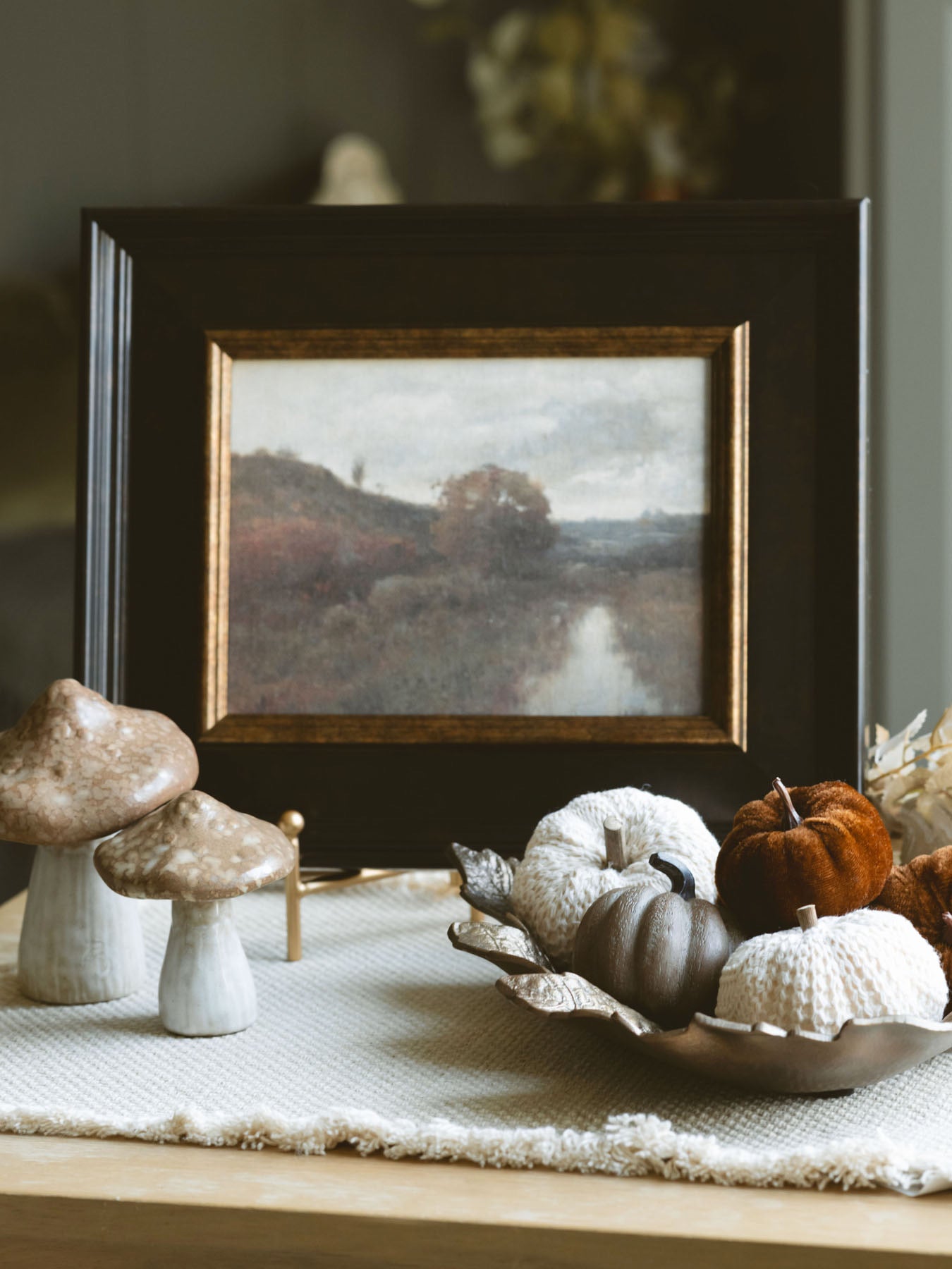 Both stoneware mushrooms styled together with a dark frame fall artwork pieces sitting on an end table. 