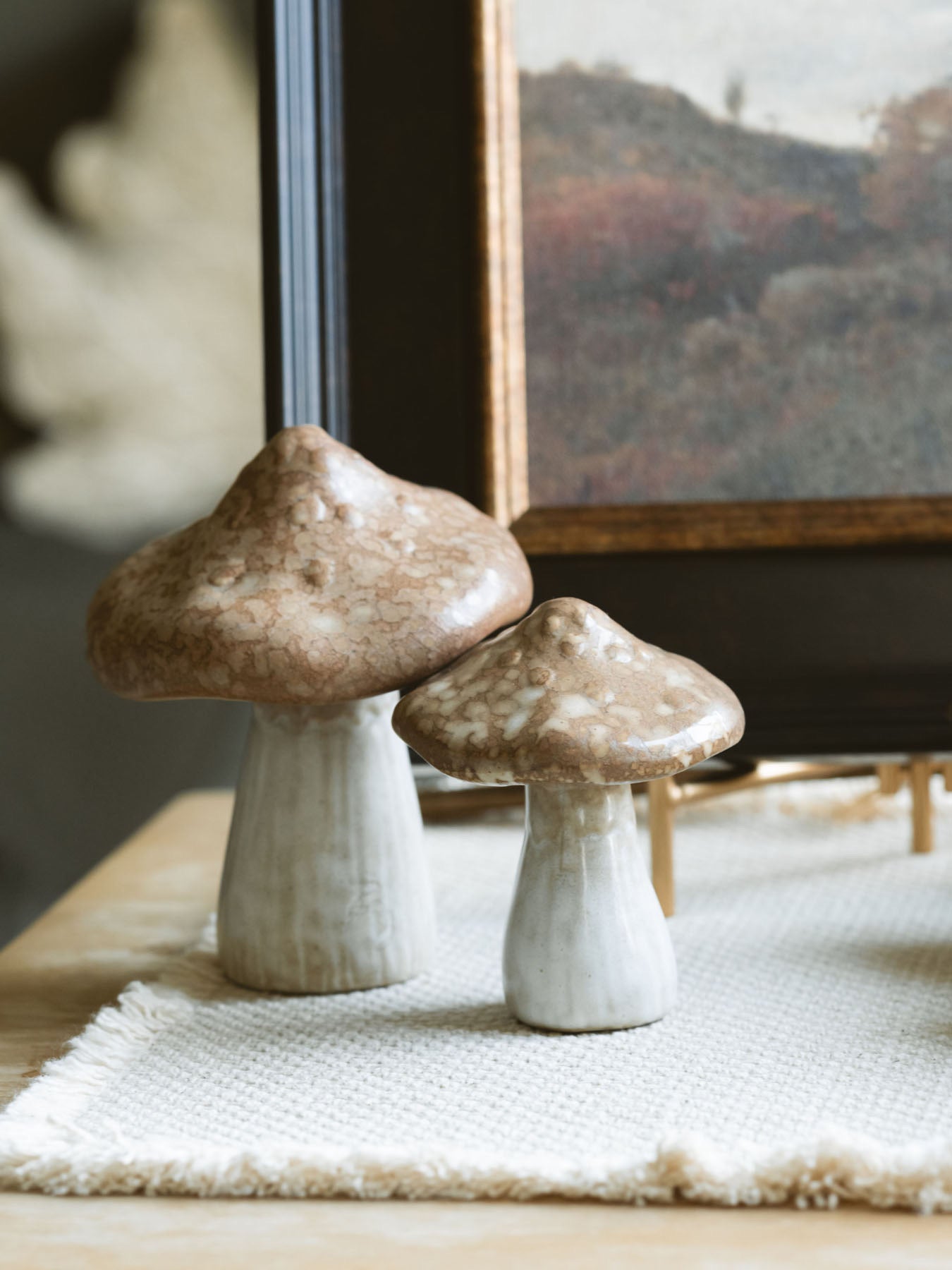 Both stoneware mushrooms styled together with a dark frame fall artwork pieces sitting on an end table. 