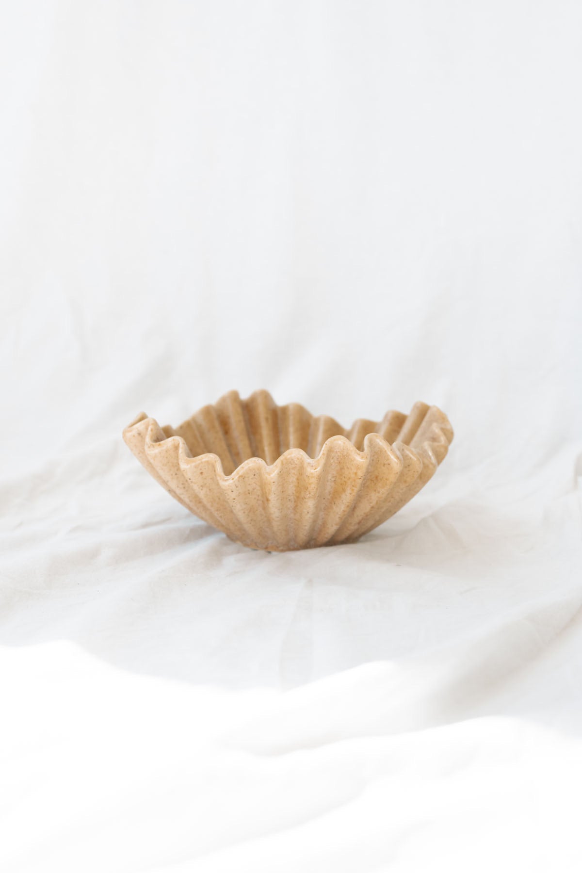 beige ruffle ceramic decorative bowl sitting against a white linen backdrop. 